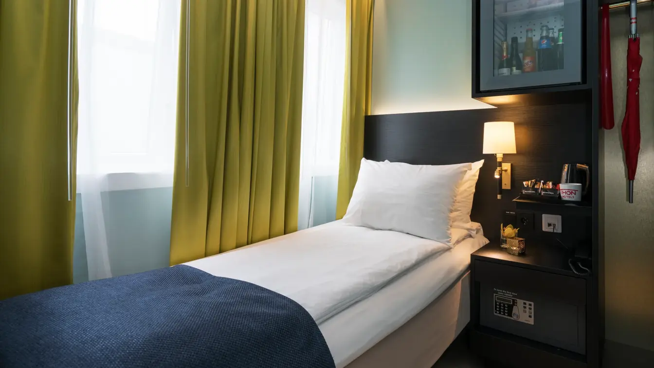 Enkeltseng med blått sengeteppe, gule gardiner og minibar på enkeltrom på Thon hotel Terminus i Oslo sentrum nær Jernbanetorget