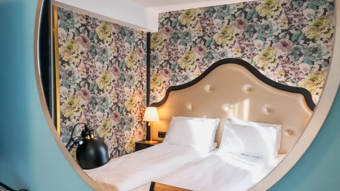 Speilbilde av blomstret tapet og dobbeltseng i dobbeltrom på Thon Hotel Cecil i Oslo sentrum
