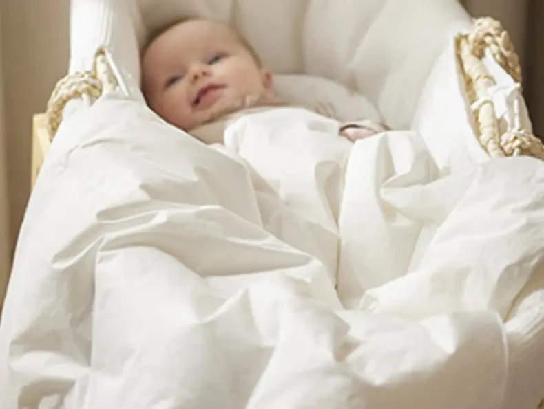 Baby i hvit babynest med sengetøy