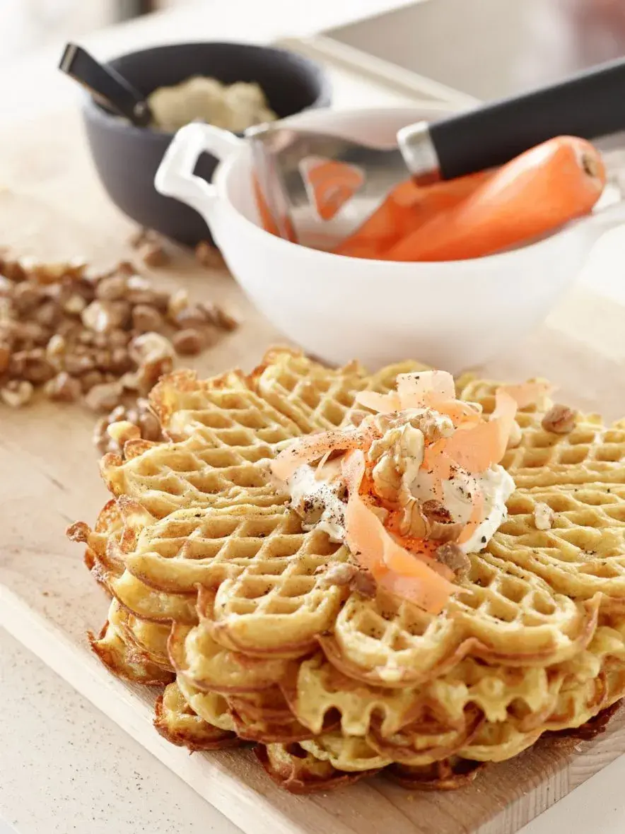 Vafler på trefjøl med raspet gulrot og nøtter på, bolle i bakgrunn med gulrøtter oppi