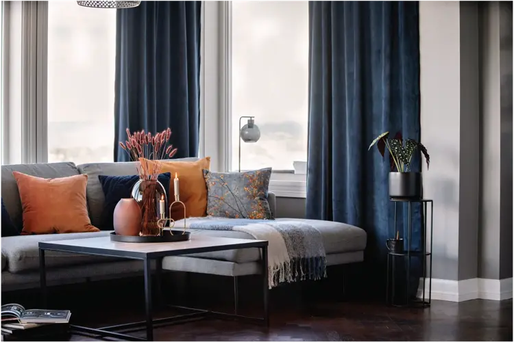 Sofagruppe med oransje puter og blå gardiner i bakrunn