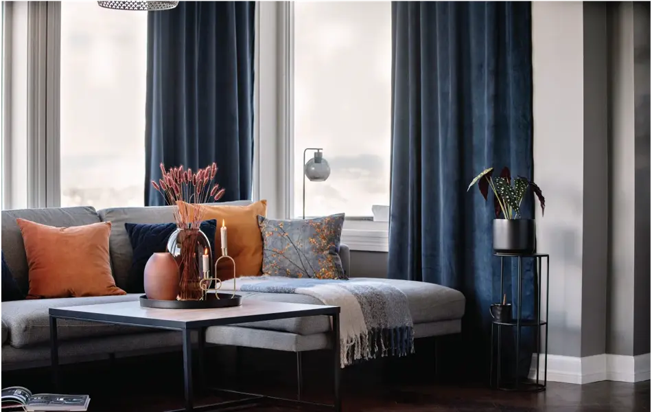 Sofagruppe med oransje puter og blå gardiner i bakrunn