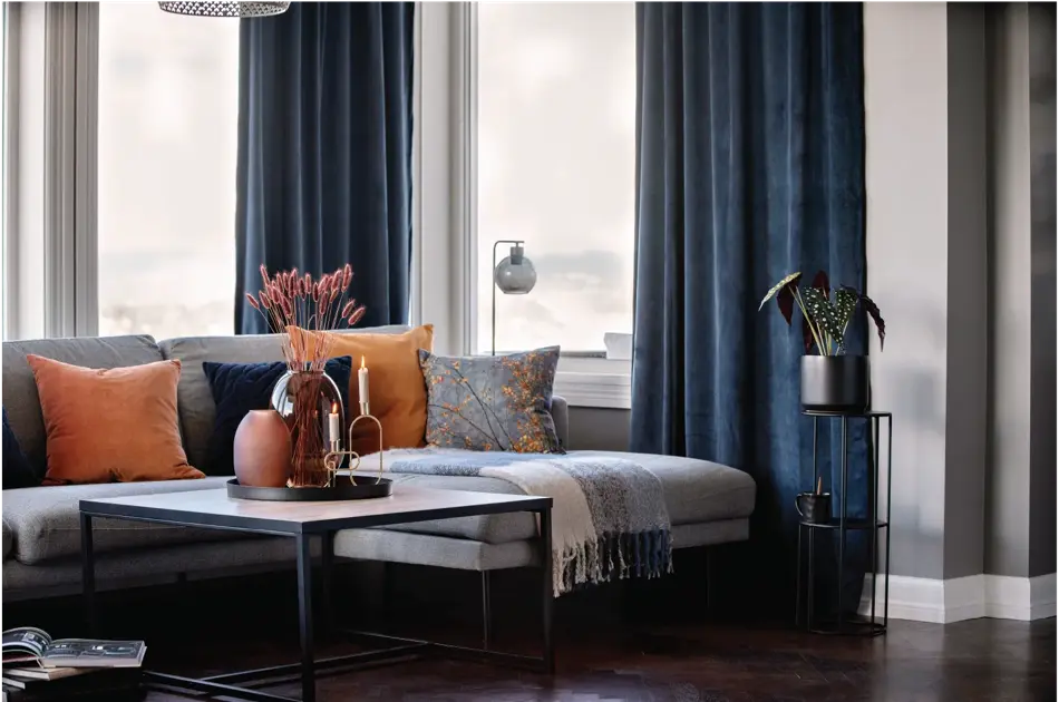 Sofagruppe med oransje puter og blå gardiner i bakrunn