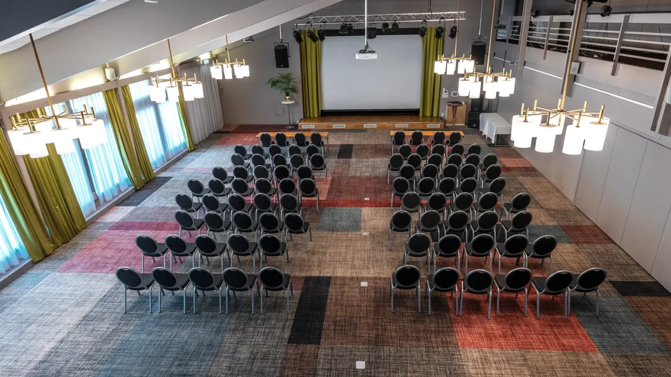 Stor sal med kino oppsett sett ovenfra, lysekroner i taket, store vinduer med gule gardiner, stort lerret foran i lokalet