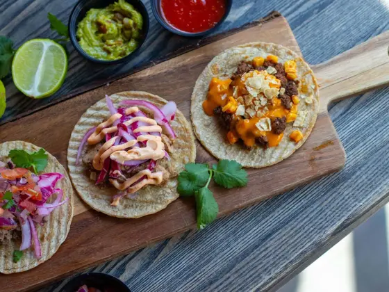 brett med tre ulike taco lefser, dekorert med lime, guacamole, dip, agurk og andre urter