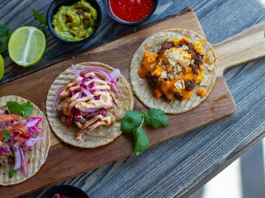 brett med tre ulike taco lefser, dekorert med lime, guacamole, dip, agurk og andre urter