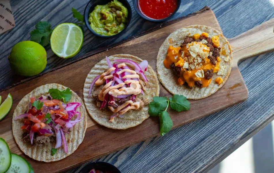 brett med tre ulike taco lefser, dekorert med lime, guacamole, dip, agurk og andre urter