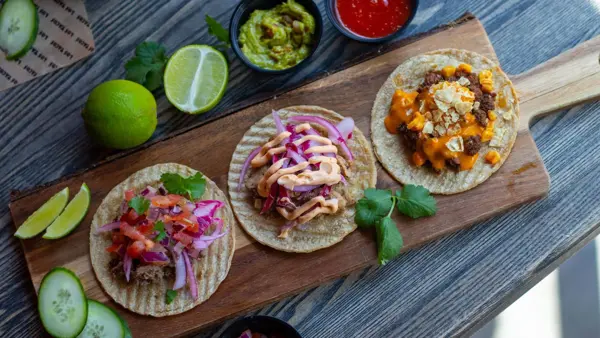 brett med tre ulike taco lefser, dekorert med lime, guacamole, dip, agurk og andre urter