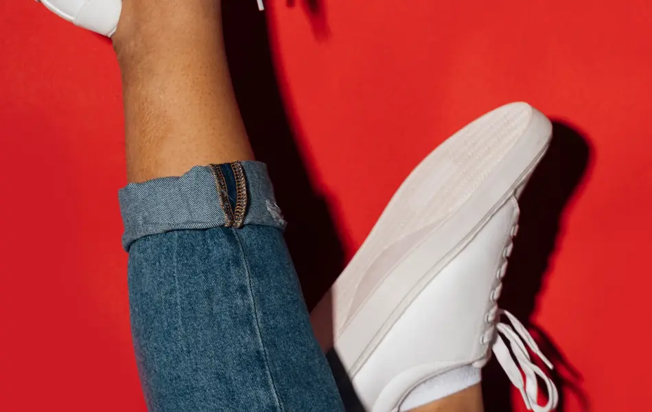 Nærbilde av manneben med hvite sneakers opp ned med rød bakgrunn