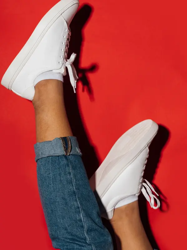 Nærbilde av manneben med hvite sneakers opp ned med rød bakgrunn