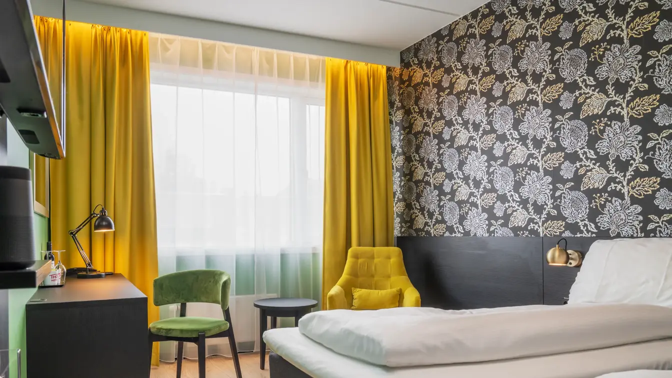 Separate senger, mørk mønstrete tapet med blomster, gule gardiner, gul stol med rundt bord og skrivebord med grønn stol i twin rom på Thon Hotel Kirkenes
