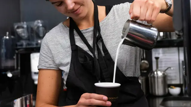 Jente som helder melk oppi en kafekopp