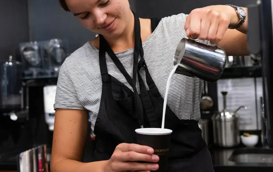 Jente som helder melk oppi en kafekopp