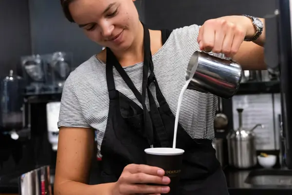 Jente som helder melk oppi en kafekopp