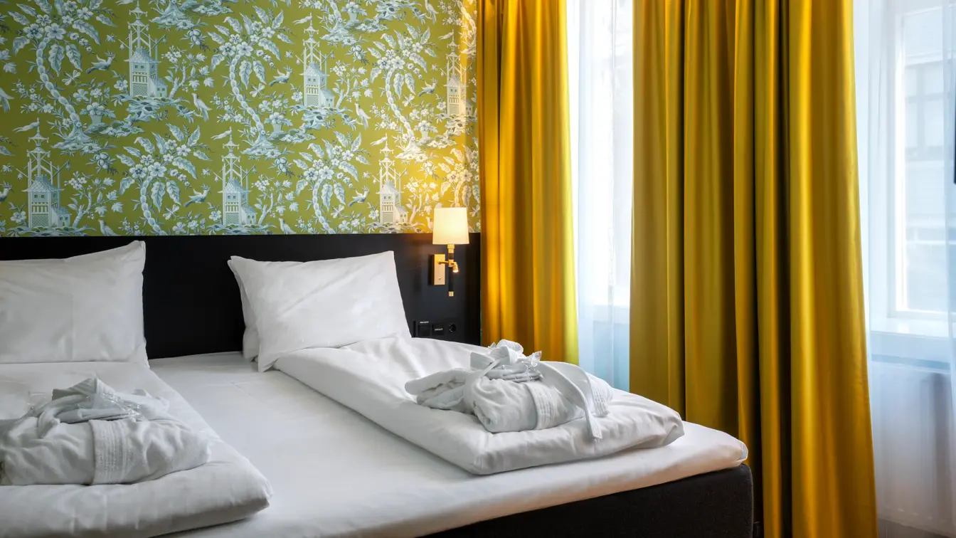 Grønn mønstrete tapet, gule store vinduer med gule gardiner og dobbeltsend med morgekåper på i junior suite på Thon Hotel Maritim.