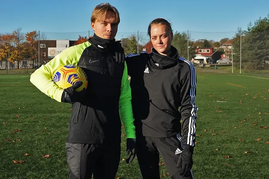 En gutt og en jente står ute på en fotballbane og holder rundt hverandre