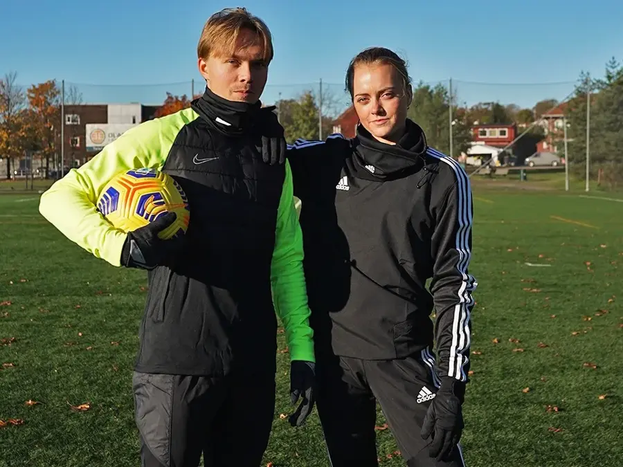 En gutt og en jente står ute på en fotballbane og holder rundt hverandre