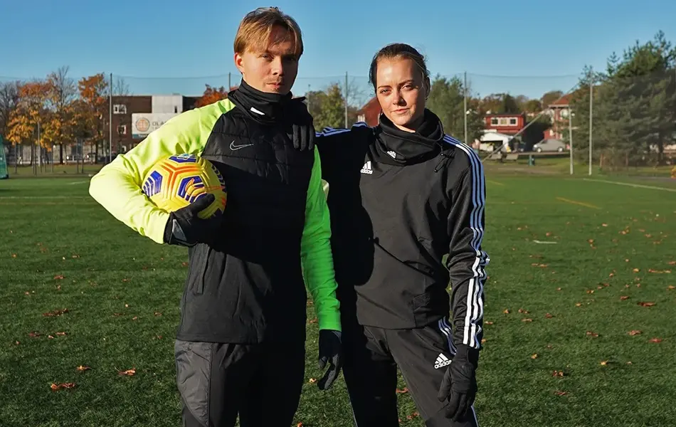 En gutt og en jente står ute på en fotballbane og holder rundt hverandre