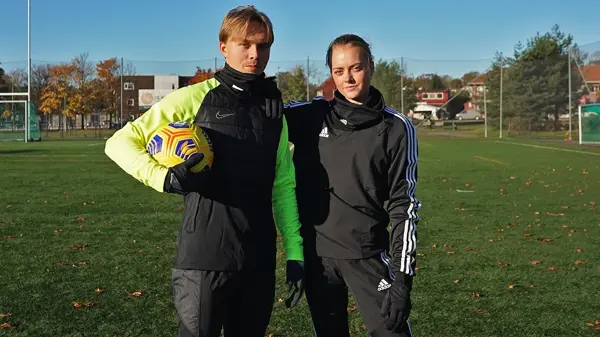 En gutt og en jente står ute på en fotballbane og holder rundt hverandre