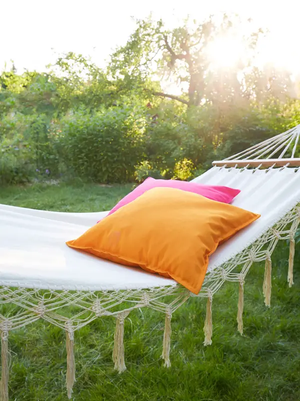 Nærbilde fra hage i soloppgang, med daghengekøye med rosa og oransje pute.