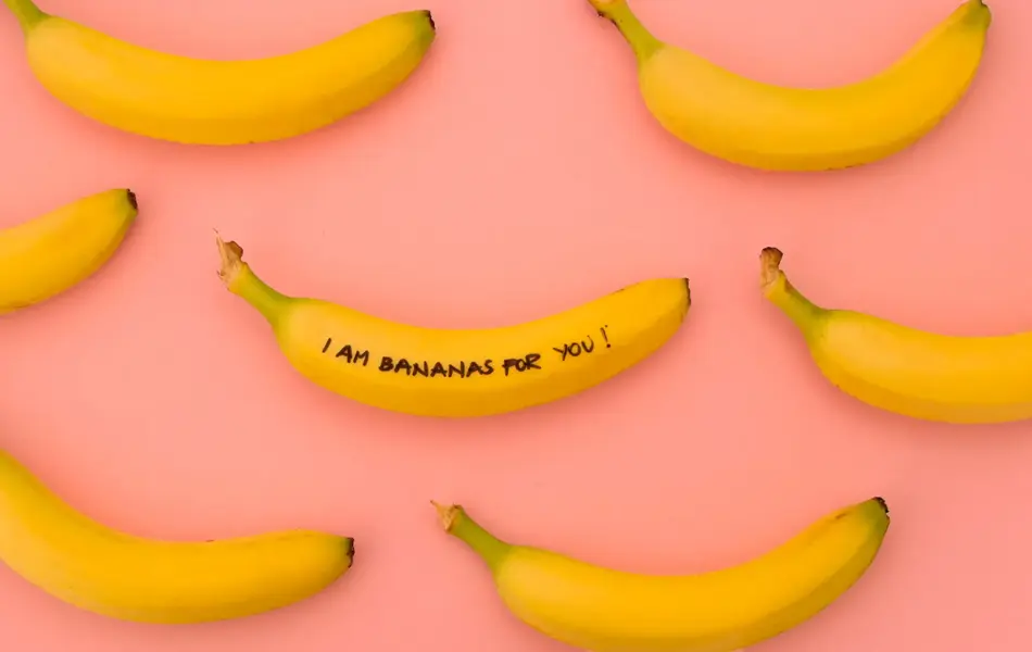 Syv gule bananer på rosa bakgrunn, på den midterste bananen står det "I am bananas for you!"