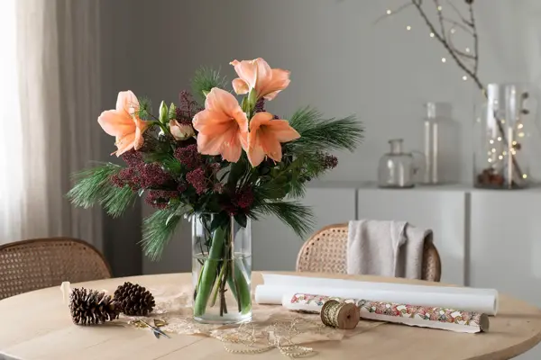 Vase med bukett av amaryllis og grønne grener.