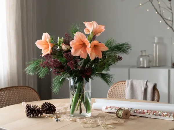 Vase med bukett av amaryllis og grønne grener.