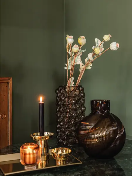 Vase med blomster og tent lys med grønn vegg i bakgrunn