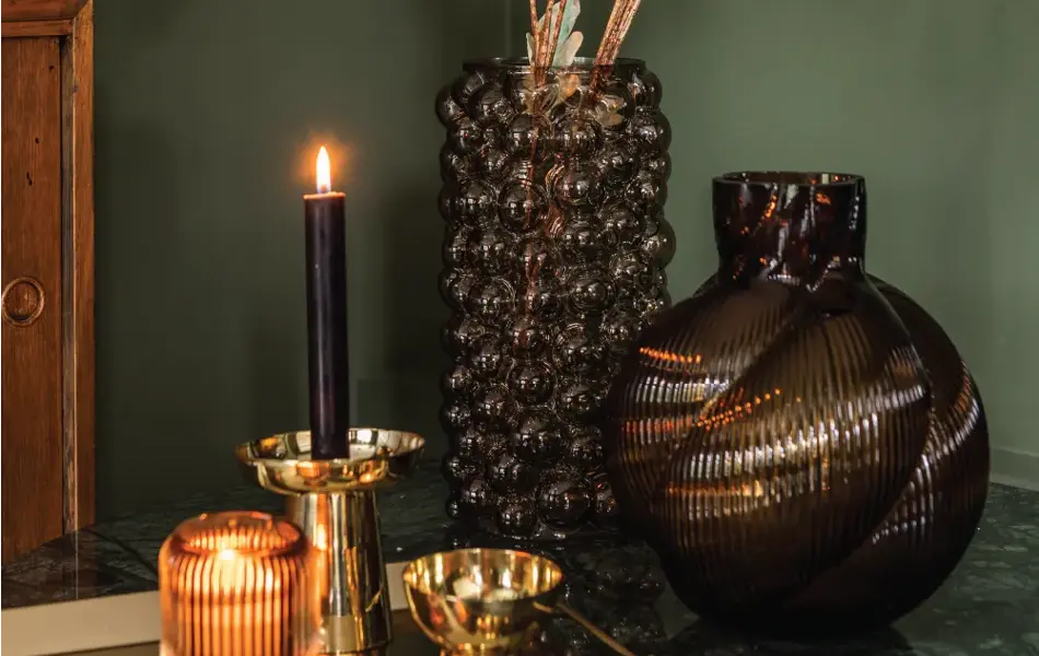 Vase med blomster og tent lys med grønn vegg i bakgrunn