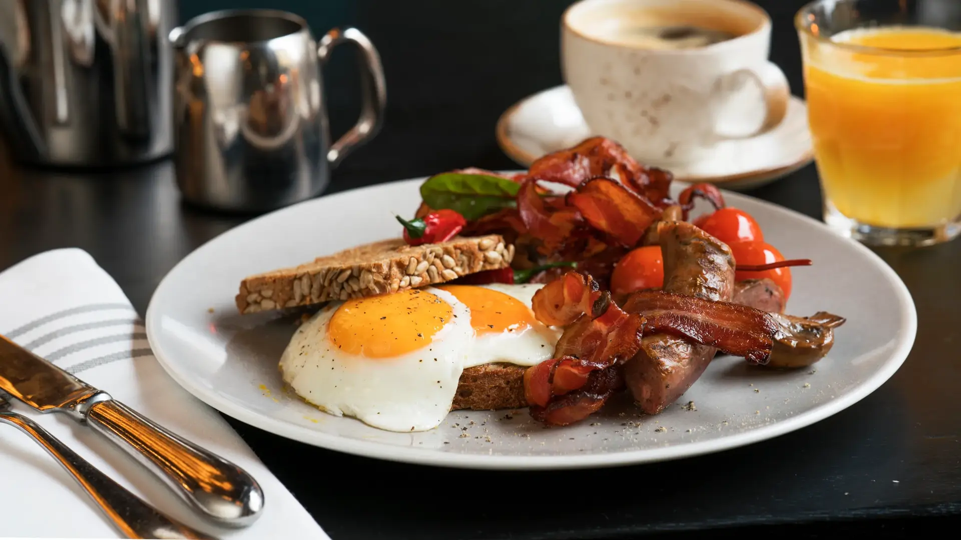 Frokosttallerken med bacon, speilegg, tomater og brødskive. Sammen med en koppkaffe og et glas ferskpresset apelsinjuice