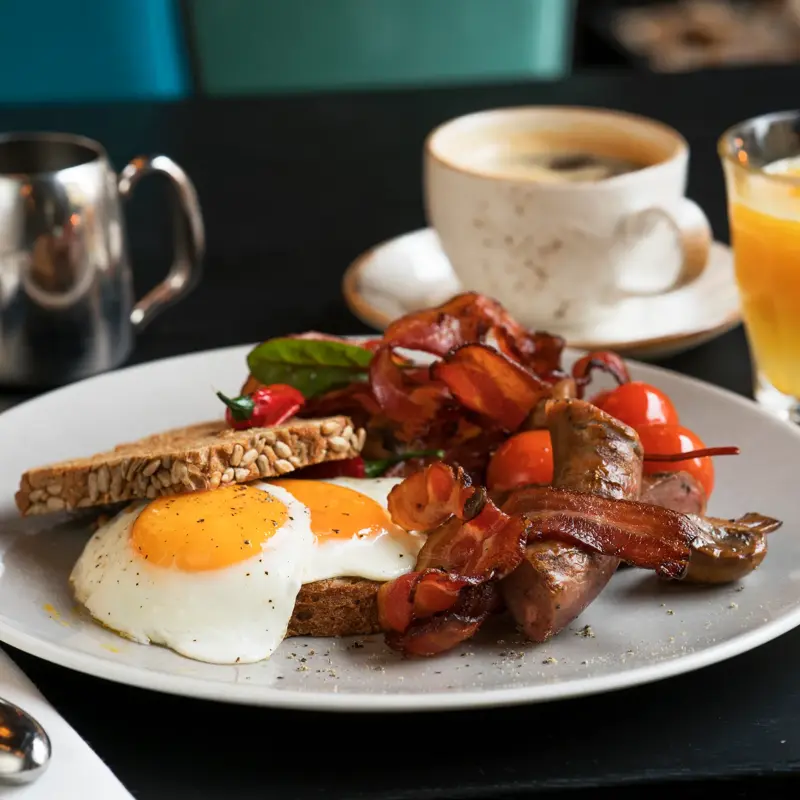 Frokosttallerken med bacon, speilegg, tomater og brødskive. Sammen med en koppkaffe og et glas ferskpresset apelsinjuice