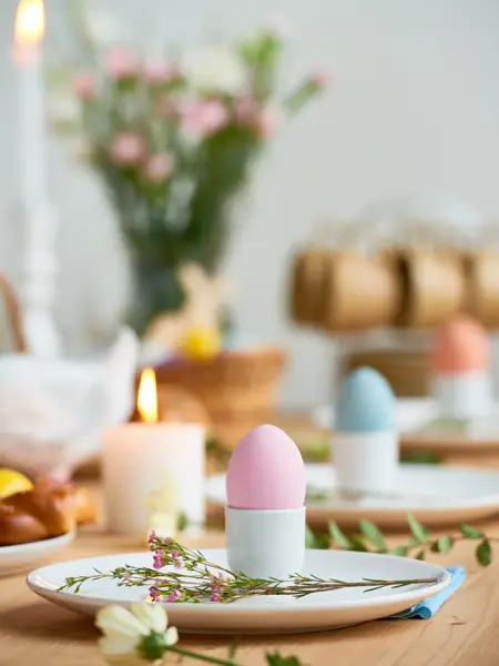 Close-up shot of plates beautifully decorated with colorful Easter eggs in cups and field flowers on blurred background of picturesque decor attributes