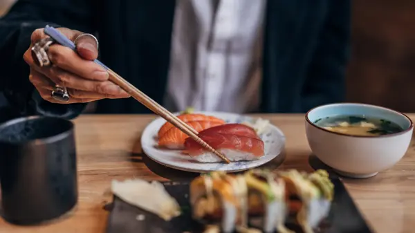 One man, gentleman sitting in restaurant alone, he is eating sushi.