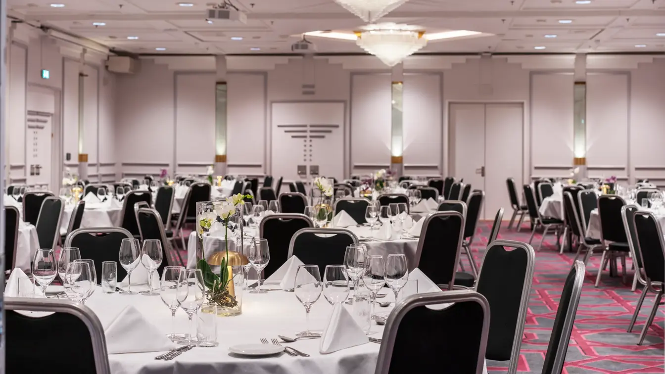 Bankett oppdekk med runde bord, hvite duker, svarte stoler, lysekroner i taket.