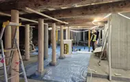 Takbjelker, nye og gamle trepæler, betongpæler og -vegg, presenning på gulv. Del av totalrenovering av Kjøpmannsgata 15 i Trondheim.
