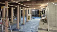 Takbjelker, nye og gamle trepæler, betongpæler og -vegg, presenning på gulv. Del av totalrenovering av Kjøpmannsgata 15 i Trondheim.