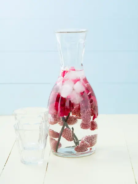 Infused water with raspberries, rose petals and vanilla beans in a pitcher