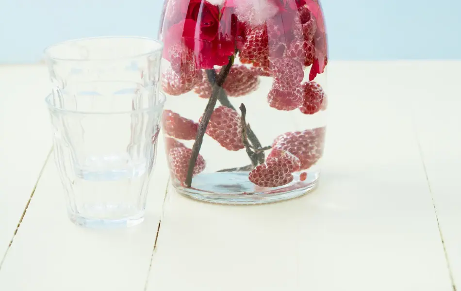 Infused water with raspberries, rose petals and vanilla beans in a pitcher