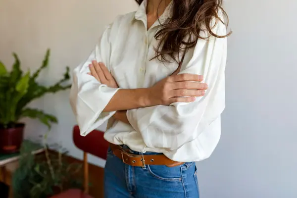 Nærbilde av dame med hvit skjorte og jeans stående med hendene i kors 