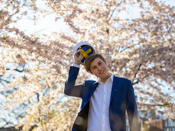 En tenåringsgutt i dress og en svensk studentlue. Han står under kirsebærtrær.