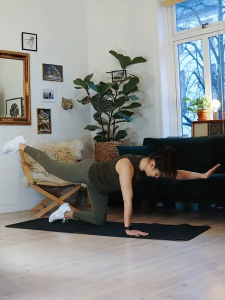treningsekspert Anna Johansen trener på matte på gulvet, mørkegrønn sofa i bakgrunnen, lys stol med pels oppi, str grønn plante, bilder på veggen