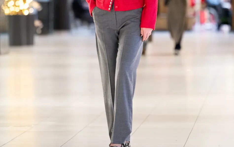 Dame med gråbukse, pums og rød jakke med glitterdetljer.