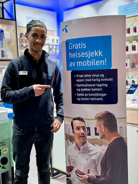 Mann fra telenorbutikken som står foran et skilt hvor det står skrevet "Gratis helsesjekk av mobilen!"