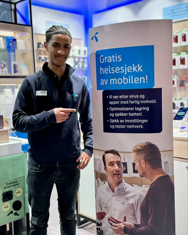 Mann fra telenorbutikken som står foran et skilt hvor det står skrevet "Gratis helsesjekk av mobilen!"