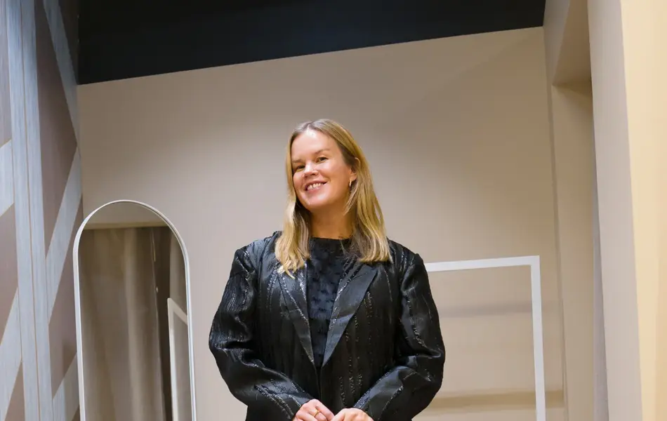 Dame med sort kjole, sort lang jakke, liten mønstret veske og sorte meshsko.