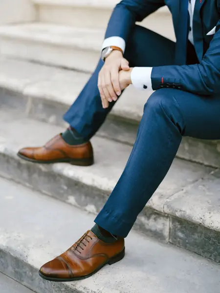 Nærbilde av gutt i blå dress med brune sko, klokke og mansjettknapper, som sitter i trapp. Foto til artikkel om kjøp av konfirmasjonsdress. 