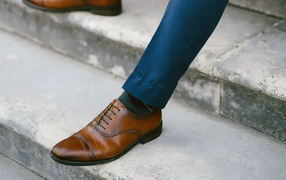 Nærbilde av gutt i blå dress med brune sko, klokke og mansjettknapper, som sitter i trapp. Foto til artikkel om kjøp av konfirmasjonsdress. 