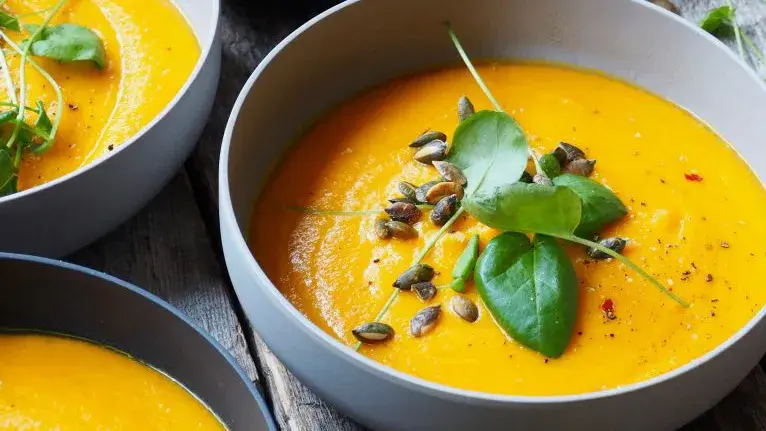 Nærbilde av skåler med gresskarsuppe pyntet med basilikum