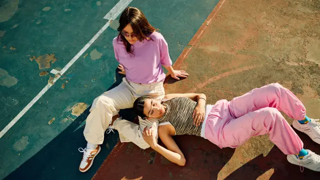 Bilde i fugleperspektiv på to damer i lyse og rosa klær som sitter på bakken