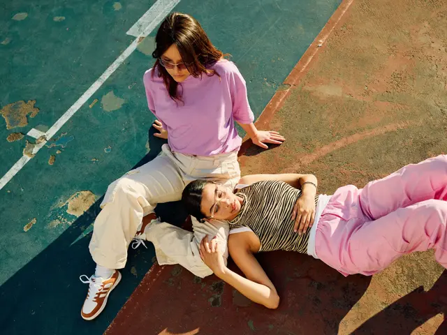 Bilde i fugleperspektiv på to damer i lyse og rosa klær som sitter på bakken